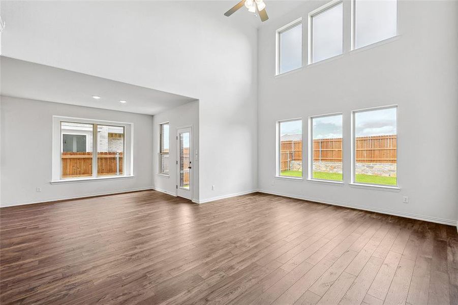 Unfurnished living room featuring hardwood / wood-style flooring, a towering ceiling, and ceiling fan