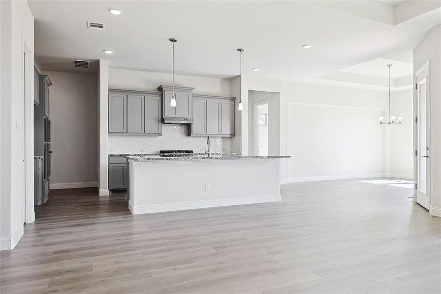 Kitchen featuring backsplash, pendant lighting, an island with sink, and gray cabinets