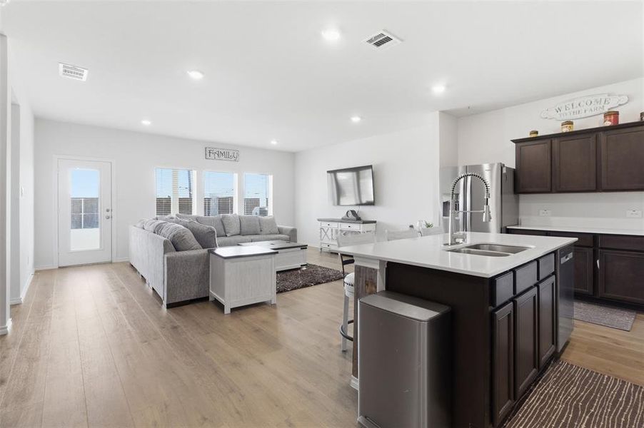 Kitchen with a kitchen island with sink, open floor plan, light wood-type flooring, dark wood finish cabinets, and recessed lighting Kitchen with a kitchen island with sink, open floor plan, light wood-type flooring, dark wood finish cabinets, and recessed lighting