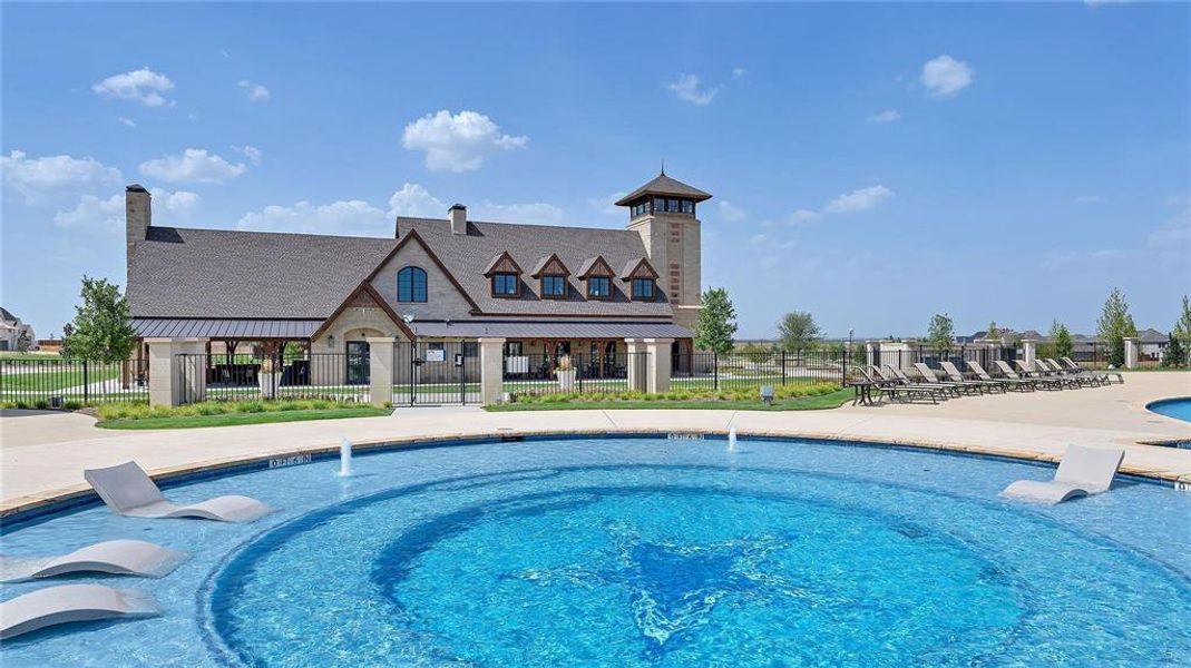 Resort-style pool with integrated sun shelves and water features, set against a clubhouse with stone and siding accents, a prominent tower, and ample patio seating