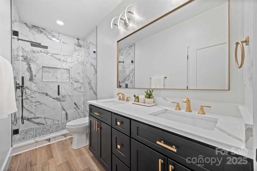The Second Full Bath showcases a modern  and elegant design with a shophisticated palette of white, black and gold elements creating a luxurious feel