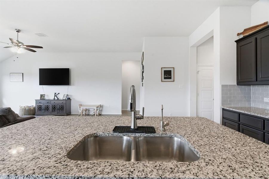 Kitchen with open floor plan, light stone countertops, lofted ceiling, decorative backsplash, and ceiling fan