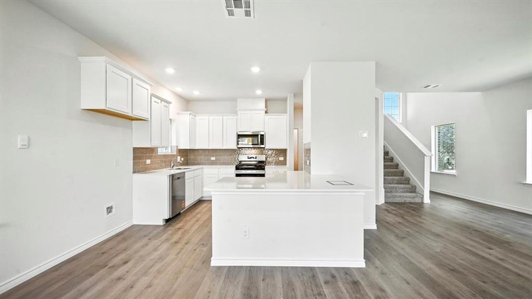 Kitchen featuring white cabinets, decorative backsplash, appliances with stainless steel finishes, light wood-style flooring, and recessed lighting