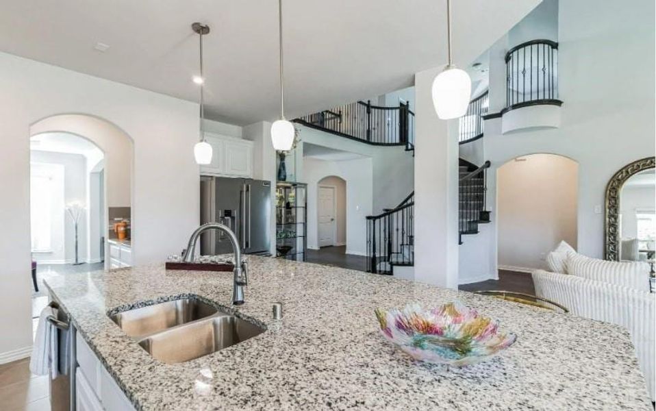 Kitchen with a high ceiling, light stone countertops, white cabinetry, and sink