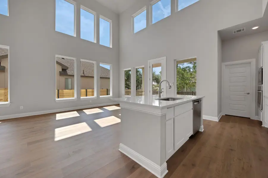 Kitchen with dark wood-style flooring, white cabinets, open floor plan, and an island with sink