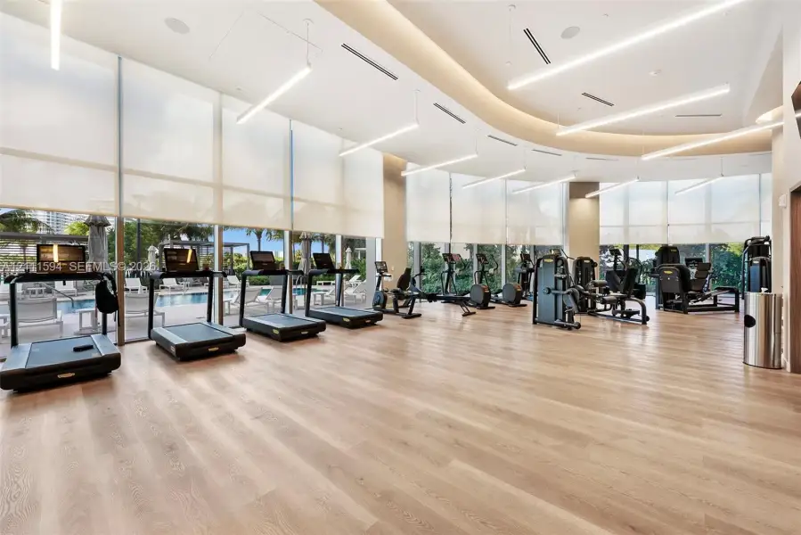 Fitness center featuring floor-to-ceiling windows, wood-finish flooring, recessed lighting, and linear suspended light fixtures Fitness center featuring floor-to-ceiling windows, wood-finish flooring, recessed lighting, and linear suspended light fixtures