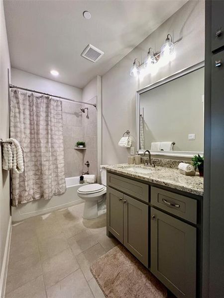 Full nice sized guest bathroom just off of the foyer featuring tile flooring, vanity, toilet, and shower / bath combo with granite countertops.