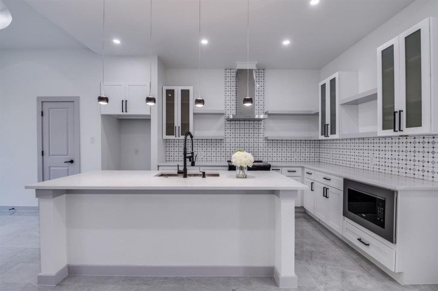 Kitchen with decorative light fixtures, wall chimney range hood, and an island with sink