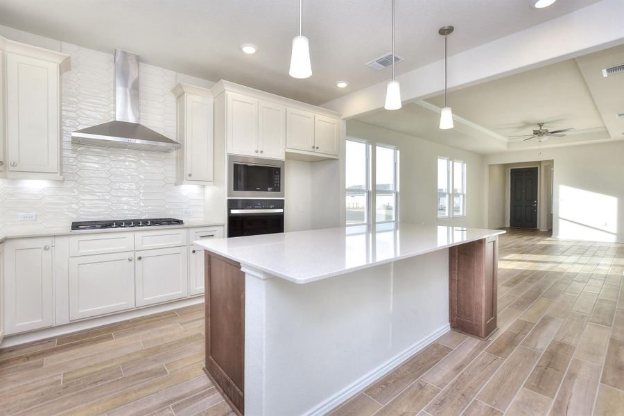 Kitchen featuring wood finish floors, visible vents, black oven, stainless steel gas stovetop, and wall chimney exhaust hood