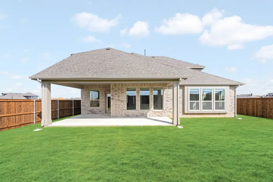 Rear exterior of brick home with covered patio, large backyard, and wood privacy fence