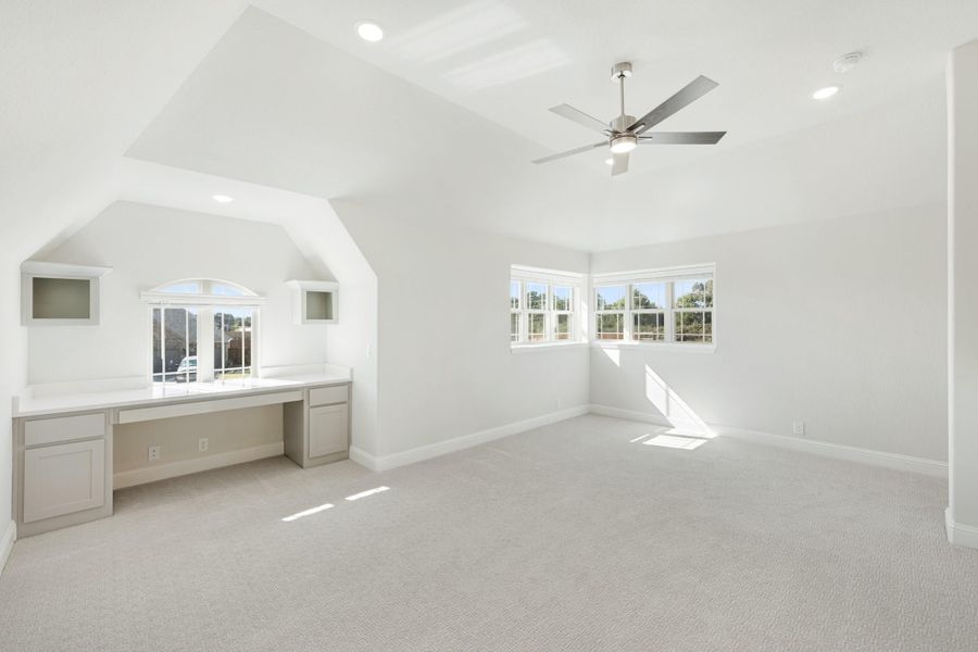 Spacious bedroom with vaulted ceiling, built-in desk, ceiling fan, and carpet flooring