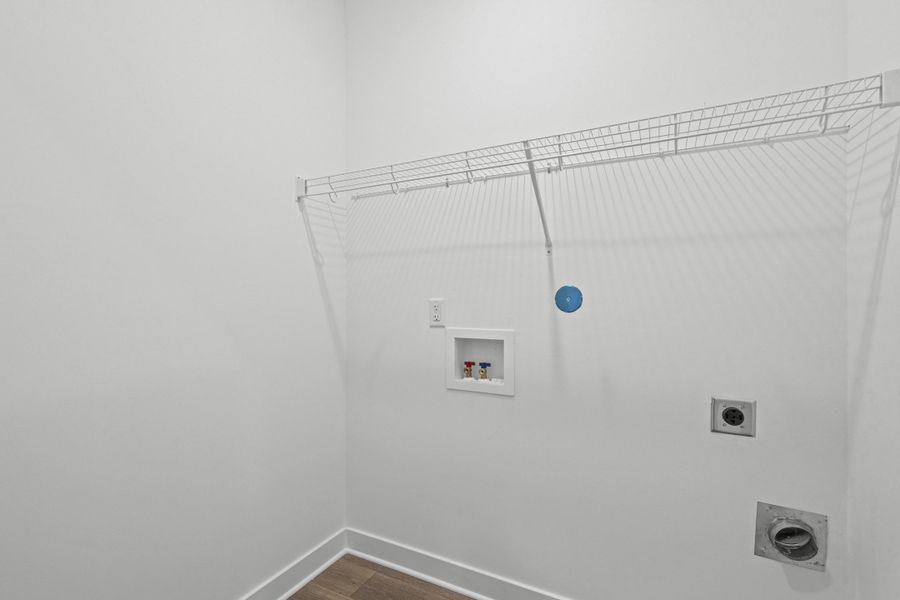 Laundry area featuring wood-finish flooring, white walls, and a wire shelf for storage