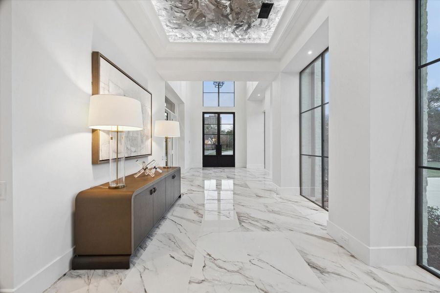 Striking foyer with floor-to-ceiling windows offering a view of the pool and front yard, filling the space with natural light and a sense of openness.
