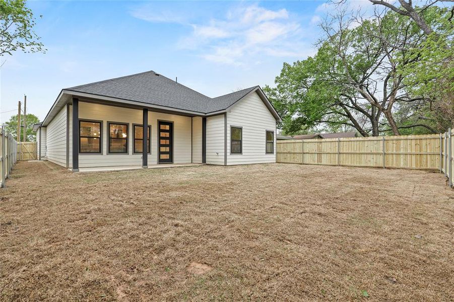 Rear view of property featuring a fenced backyard, a shingled roof, and a lawn