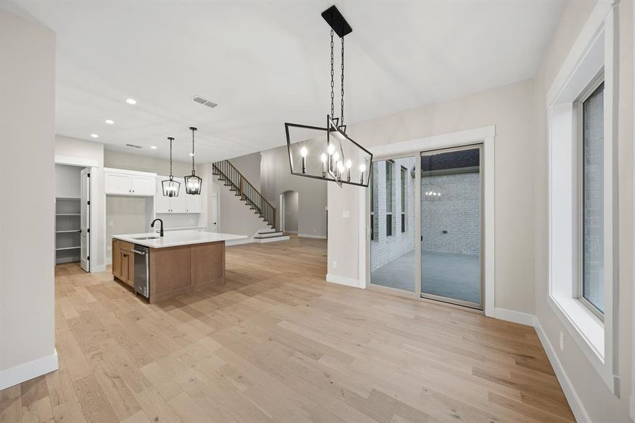 Kitchen with a chandelier, open floor plan, light wood-type flooring, a kitchen island with sink, and hanging light fixtures