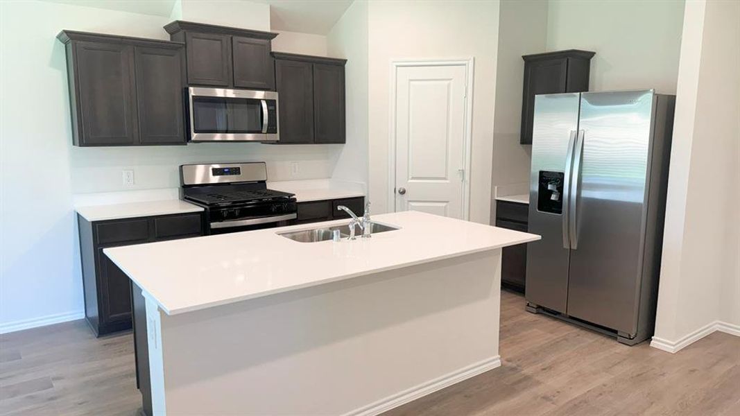 Kitchen with stainless steel appliances, a kitchen island with sink, light wood finished floors, and light stone counters