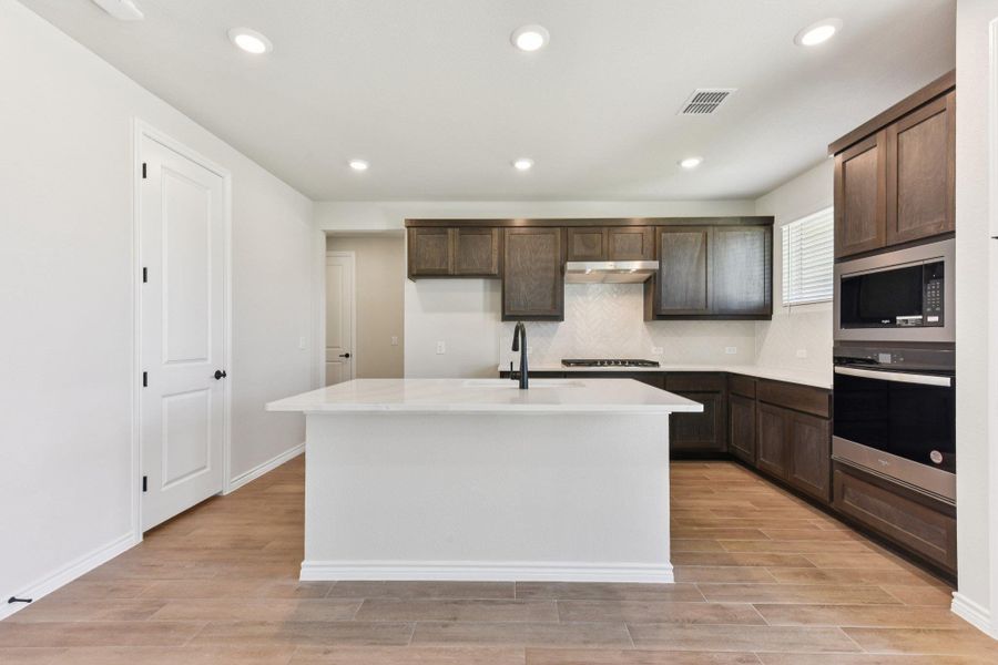 Kitchen with wood finish floors, stainless steel appliances, recessed lighting, an island with sink, and tasteful backsplash