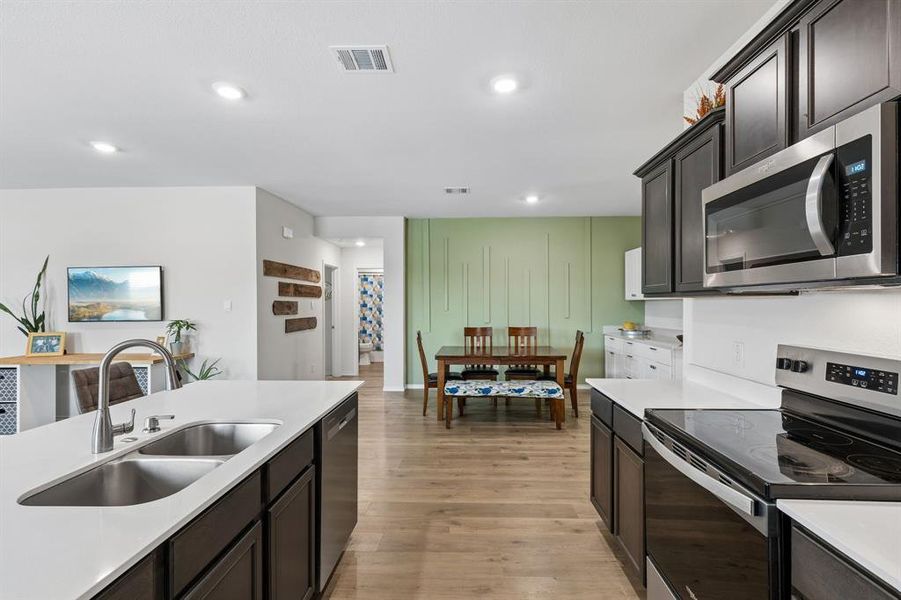 Kitchen with stainless steel appliances, dark wood finish cabinets, light wood-style flooring, recessed lighting, and light stone counters Kitchen with stainless steel appliances, dark wood finish cabinets, light wood-style flooring, recessed lighting, and light stone counters