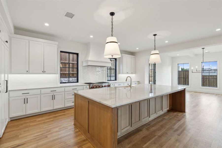 Kitchen with light hardwood / wood-style floors, white cabinets, light stone countertops, decorative light fixtures, and a spacious island