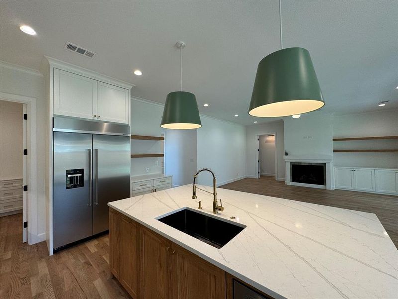 Kitchen featuring stainless steel built in refrigerator, white cabinets, light stone counters, hardwood / wood-style floors, and sink