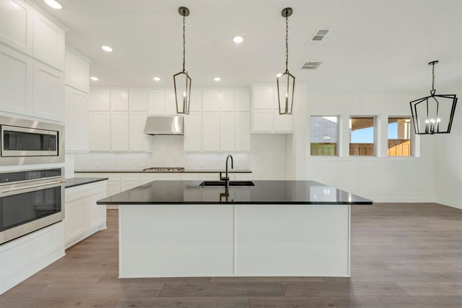 Kitchen with stainless steel appliances, light wood-style floors, white cabinetry, decorative light fixtures, and an island with sink Kitchen with stainless steel appliances, light wood-style floors, white cabinetry, decorative light fixtures, and an island with sink