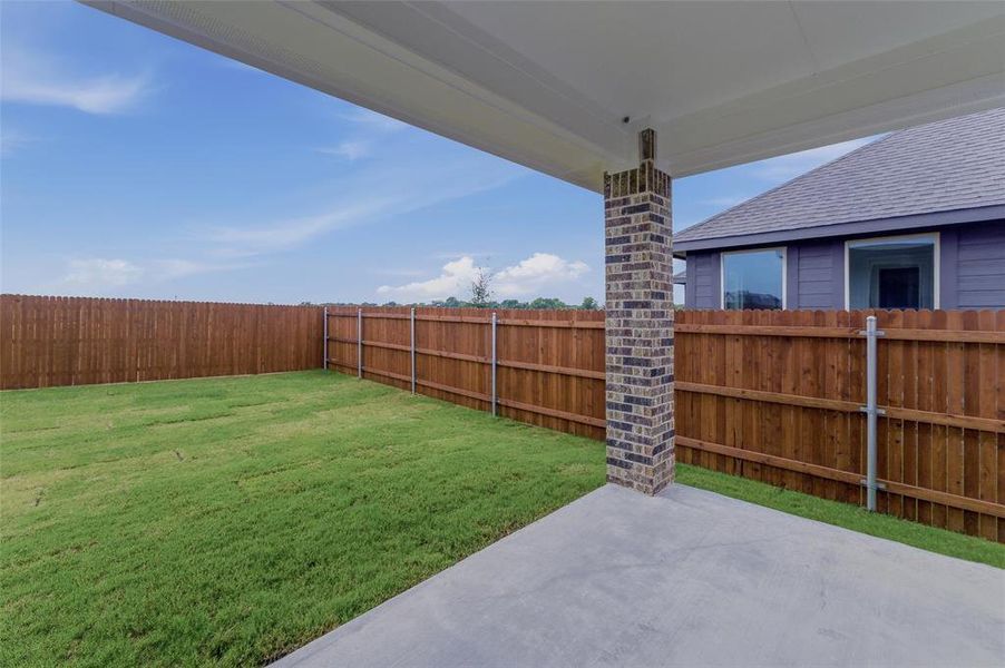 Expansive backyard featuring a concrete patio, brick support column, wood privacy fencing, and green lawn space Expansive backyard featuring a concrete patio, brick support column, wood privacy fencing, and green lawn space