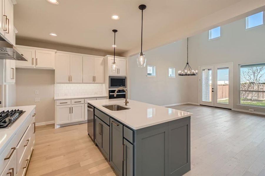 Kitchen with white cabinetry, sink, an island with sink, and hanging light fixtures