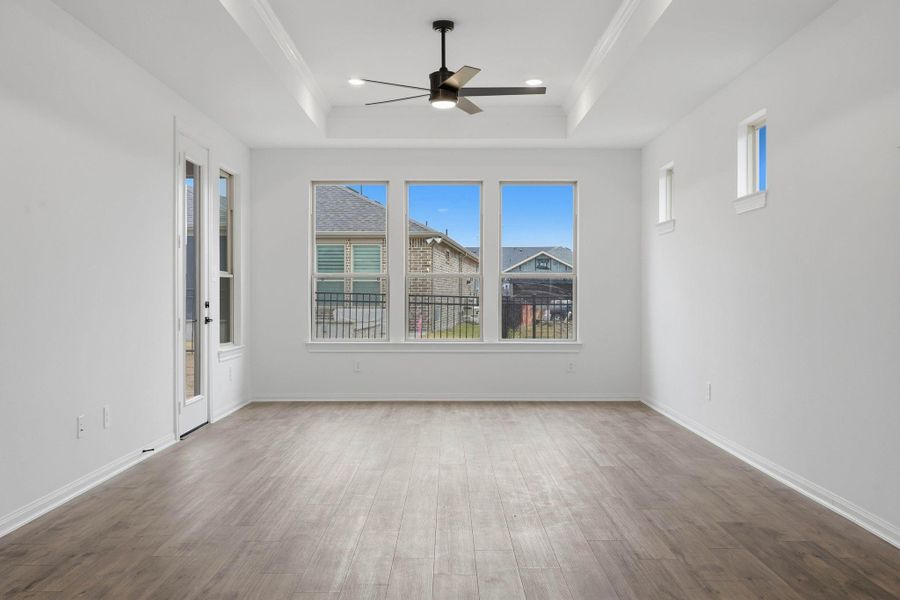Bright and spacious living room with large windows, wood flooring, and a modern ceiling fan, plus a door leading outside that brings in abundant natural light and enhances the open, inviting feel.