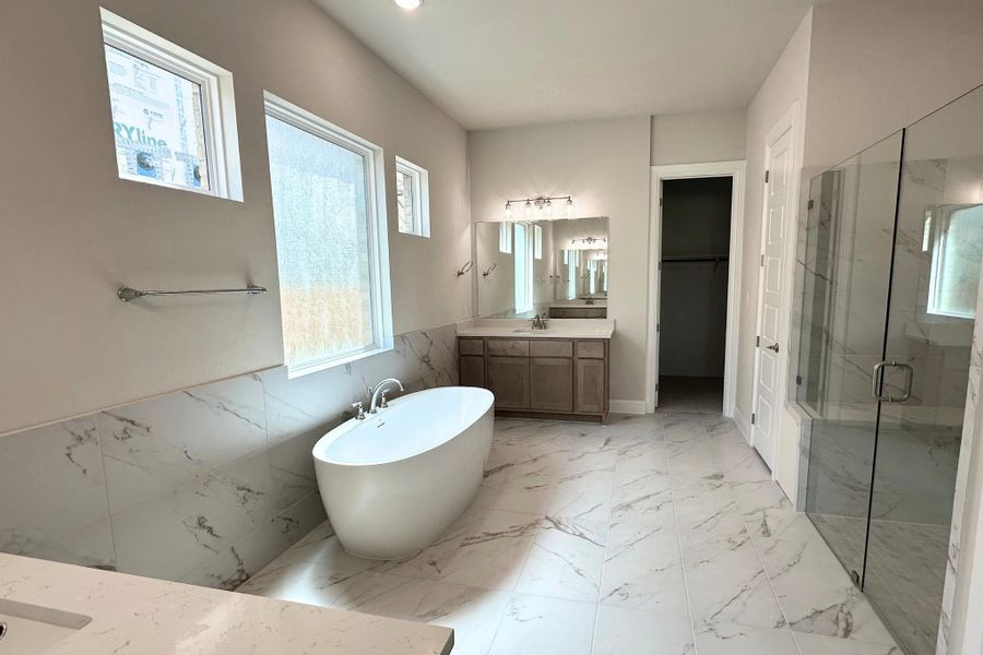 Spacious bathroom featuring a freestanding soaking tub, large format tile flooring, and a glass-enclosed shower