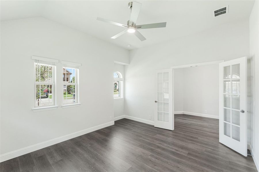 Empty room with vaulted ceiling, ceiling fan, dark hardwood floors, and white French doors Empty room with vaulted ceiling, ceiling fan, dark hardwood floors, and white French doors