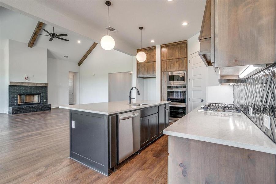 Kitchen featuring vaulted ceiling with beams, a brick fireplace, a center island with sink, and dark hardwood / wood-style floors