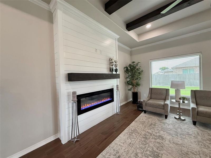 Living area with ornamental molding, dark wood-style flooring, a glass covered fireplace, recessed lighting, and beam ceiling Living area with ornamental molding, dark wood-style flooring, a glass covered fireplace, recessed lighting, and beam ceiling