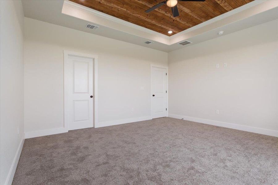 A restful bedroom with soft carpeting and a unique tray ceiling, featuring warm wood accents and an integrated fan for comfort.