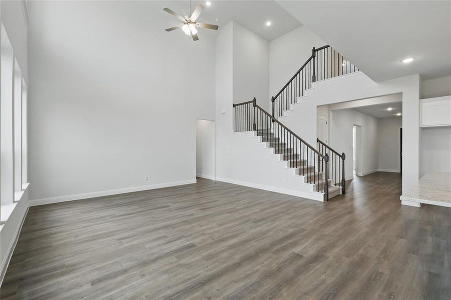 Unfurnished living room with stairway, a high ceiling, wood finished floors, baseboards, and ceiling fan