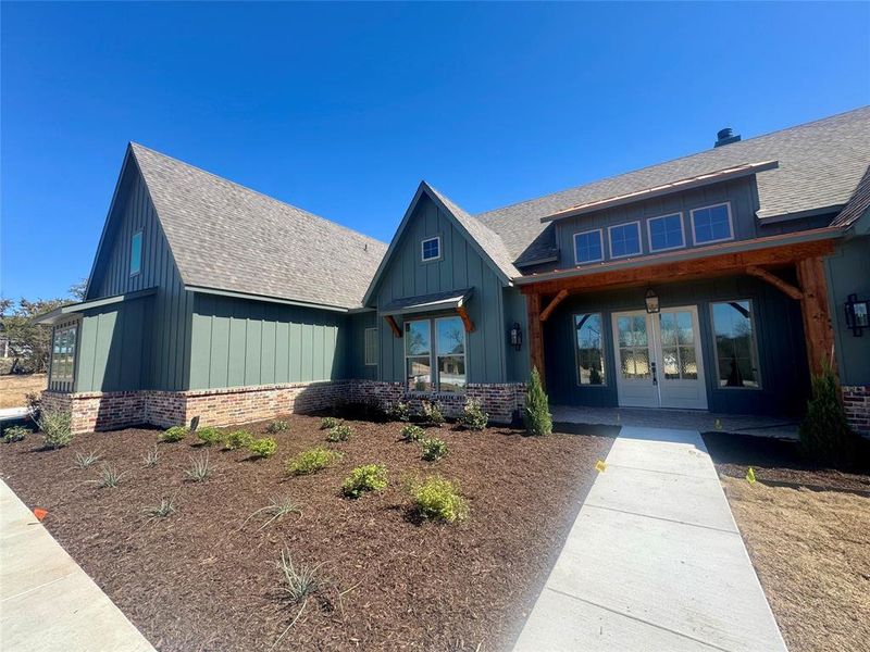 View of front of house with brick siding, board and batten siding, and roof with shingles