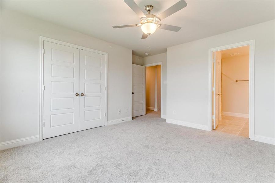 Unfurnished bedroom featuring connected bathroom, light colored carpet, a closet, and ceiling fan