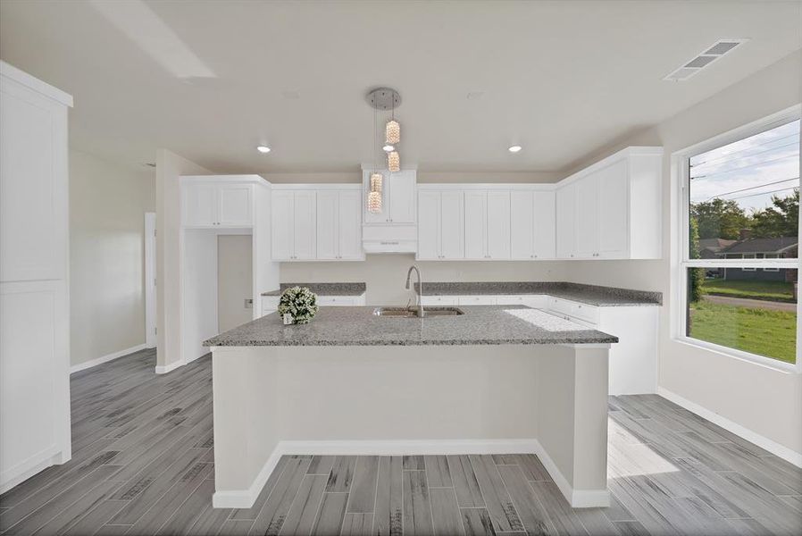 Kitchen with light wood-style flooring, a kitchen island with sink, white cabinets, light stone countertops, and recessed lighting