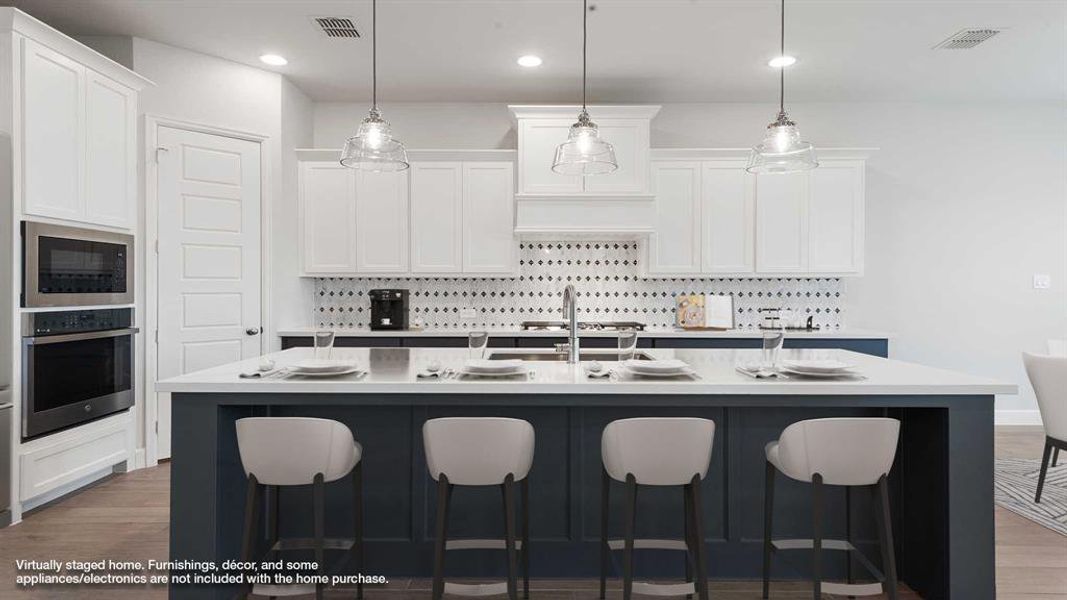 Kitchen featuring hardwood / wood-style floors, pendant lighting, a center island with sink, white cabinets, and appliances with stainless steel finishes