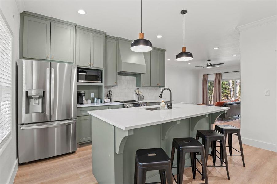 Kitchen featuring ceiling fan, stainless steel appliances, light hardwood / wood-style flooring, pendant lighting, and a breakfast bar