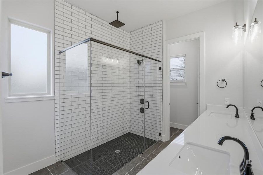 Bathroom featuring a shower stall, double vanity, and dark tile patterned flooring