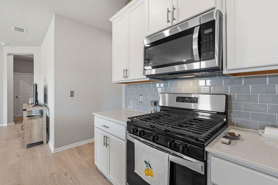 Kitchen featuring stainless steel appliances, light wood-style floors, white cabinetry, light stone countertops, and tasteful backsplash Kitchen featuring stainless steel appliances, light wood-style floors, white cabinetry, light stone countertops, and tasteful backsplash