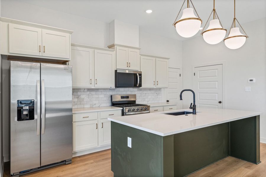 Kitchen featuring stainless steel appliances, light wood finished floors, a kitchen island with sink, decorative backsplash, and dual tone cabinetry