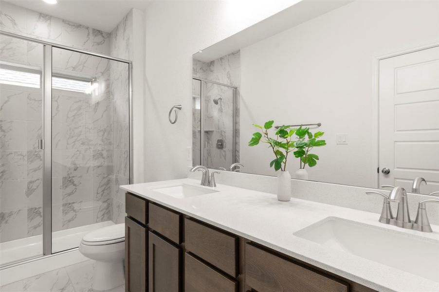 Full bath featuring double vanity, a marble finish shower, and marble look tiles