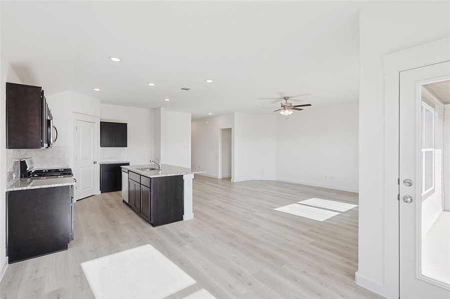 Kitchen featuring a center island with sink, ceiling fan, decorative backsplash, and light hardwood / wood-style flooring