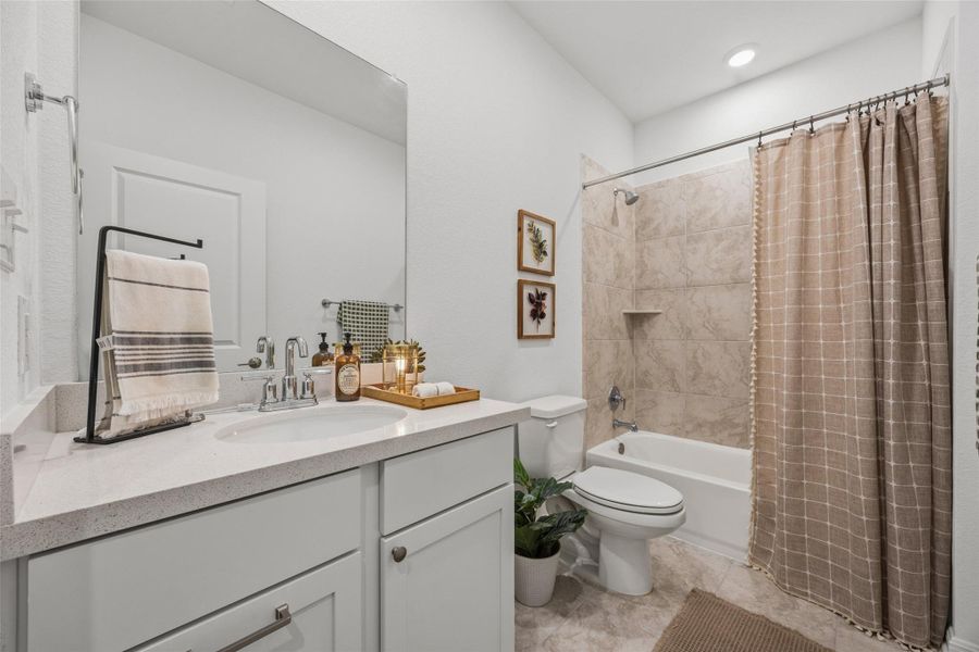 Bathroom featuring a single vanity with a white countertop and undermount sink, a large wall-mounted mirror, and a white bathtub with a tiled shower surround and built-in niche