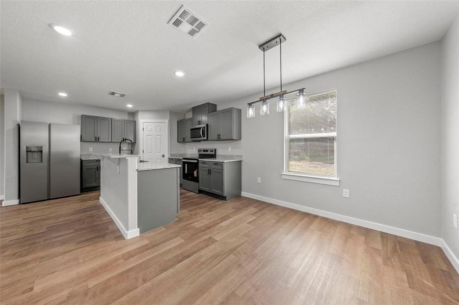Kitchen with stainless steel appliances, gray cabinets, light wood-style floors, light stone countertops, and recessed lighting Kitchen with stainless steel appliances, gray cabinets, light wood-style floors, light stone countertops, and recessed lighting