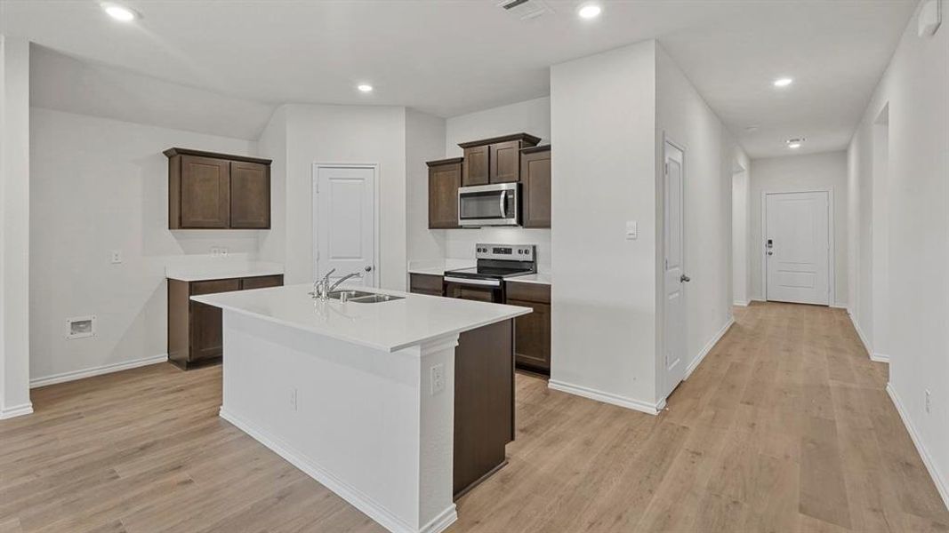 Kitchen featuring an island with a double basin sink, white countertops, dark wood cabinetry, stainless steel appliances, and recessed lighting