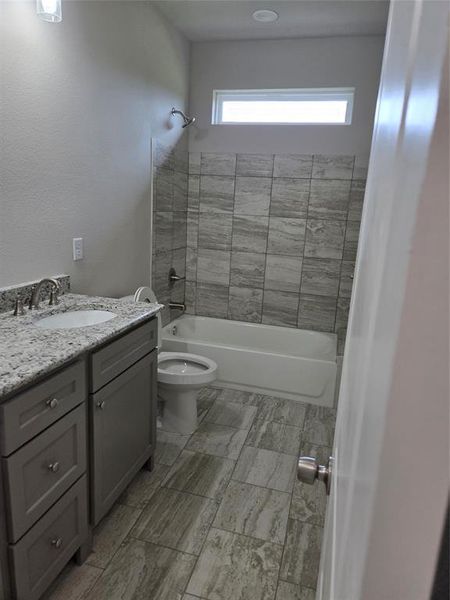 Full bathroom featuring tiled shower / bath, vanity, toilet, and tile floors