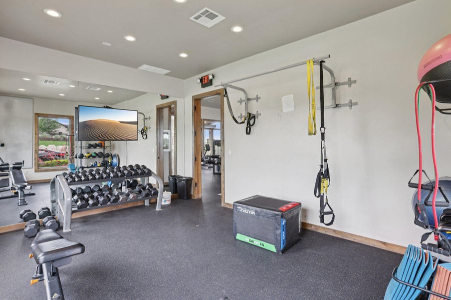 HOA maintained gym features a wide selection of free weights, a large wall-mounted mirror, and recessed lighting