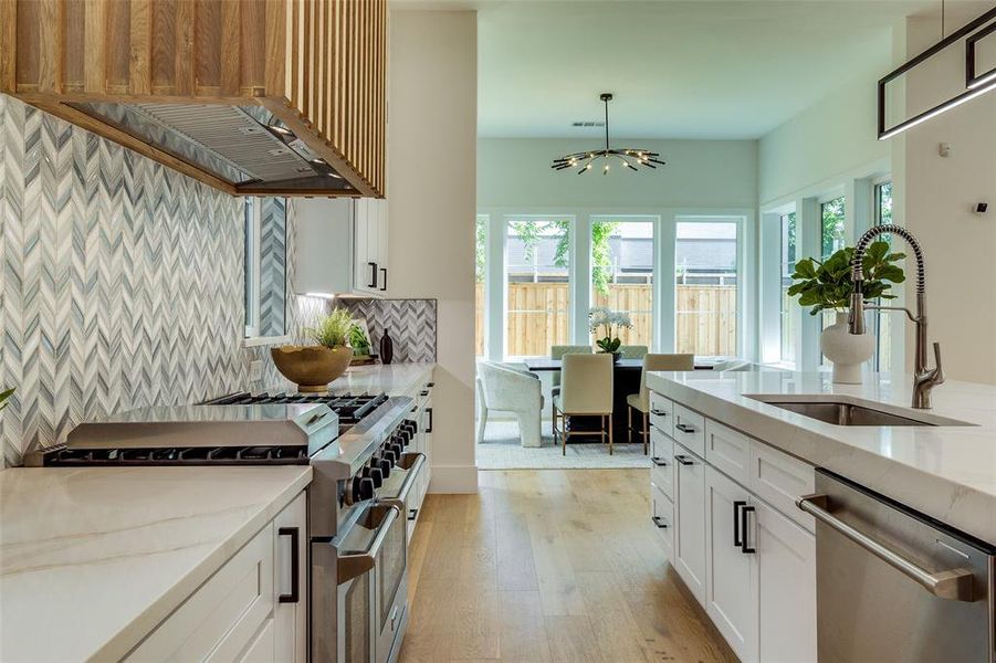 Kitchen with white cabinets, backsplash, stainless steel appliances, light hardwood / wood-style floors, and sink